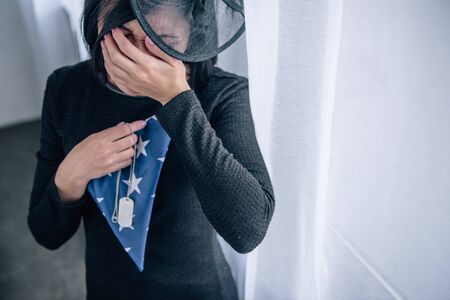 crying woman holding tag dog and folded american flag at home