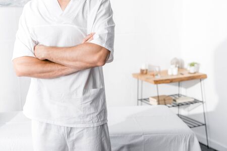 cropped view of masseur standing with crossed arms and looking at camera in clinicの写真素材