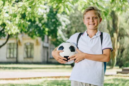 cute cheerful schoolboy holding soccer ball and smiling at cameraの写真素材