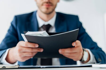 cropped view of man holding envelope with dollar banknotes near laptop on tableの写真素材