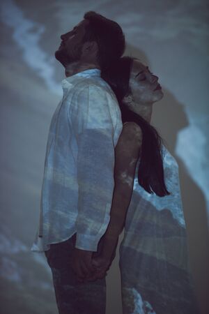 side view of man and girl standing back to back to each other in darkness