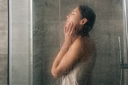 sad depressed woman in shower through glass with water dropsの写真素材