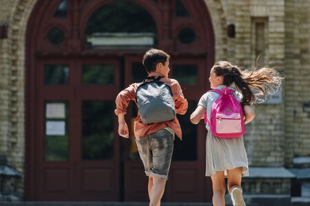 back view of two schoolkids with backpacks running in schoolyardの写真素材