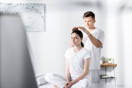 woman sitting on massage table with closed eyes while healer holding hands above her headの写真素材
