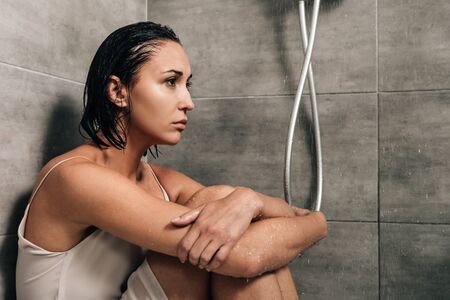 lonely upset woman sitting in shower at homeの写真素材