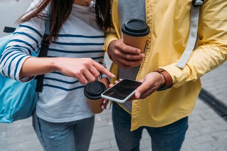 Cropped view of bi-racial man with paper cup holding smartphone and woman pointing with fingerの写真素材
