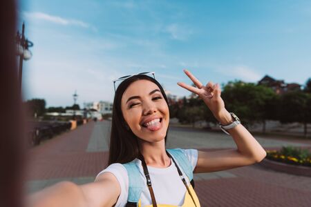attractive and asian woman taking selfie and sticking out tongue