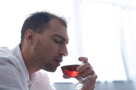 depressed man in shirt drinking cognac at homeの写真素材
