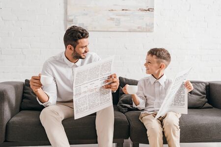 son and dad in formal wear sitting on sofa and reading newspapersの写真素材