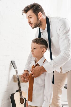 bearded dad helping son with tie at home