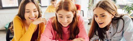 panoramic shot of three smiling girls in school