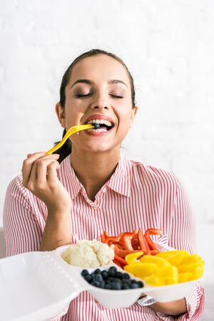 happy woman holding plastic fork with blueberry near vegetablesの写真素材