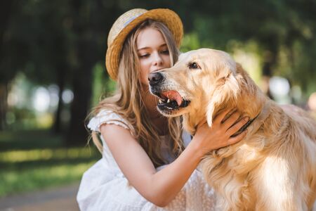 beautiful girl in white dress and straw petting golden retriever and looking at dogの写真素材