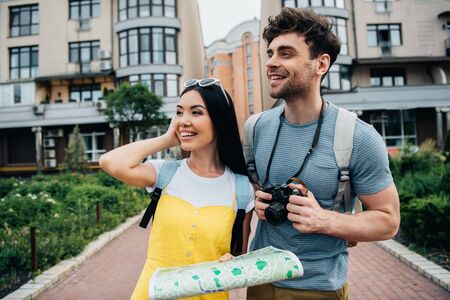 handsome man with digital camera and asian woman with map looking away