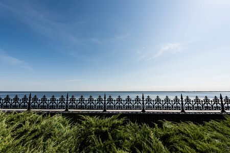 selective focus of metallic fence near green grass against blue sky