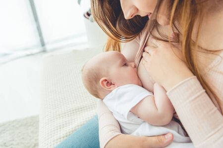 cropped view of mother breastfeeding her child in apartmentの写真素材
