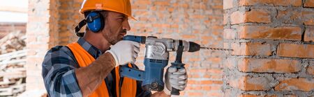 panoramic shot of handsome bearded man using hammer drill near brick wallの写真素材