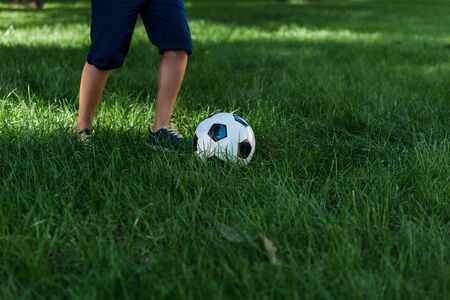 cropped view of boy playing football on green grassの写真素材