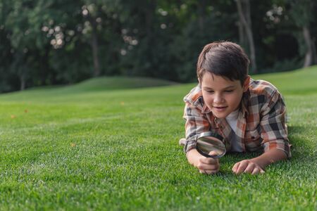 selective focus of cute boy looking at grass through magnifierの写真素材