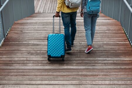 cropped view of multicultural man and woman walking with blue luggageの写真素材