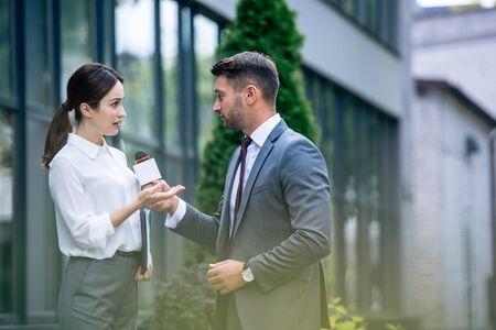 journalist holding microphone and talking with businesswoman in formal wear