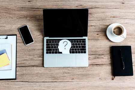 top view of smartphone near laptop with blank screen and paper human head with question mark