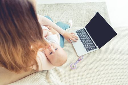 cropped view of mother holding her child and using laptop in apartmentの写真素材