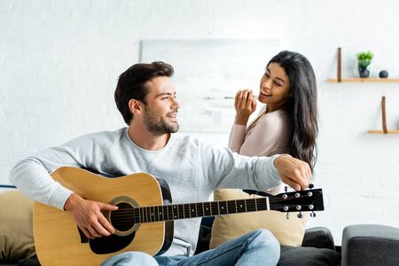 smiling african american woman looking at man with acoustic guitarの写真素材