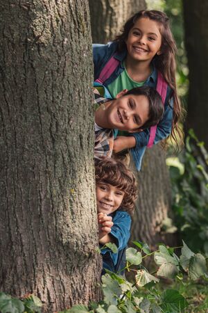 happy boys smiling near tree trunk with cute friend