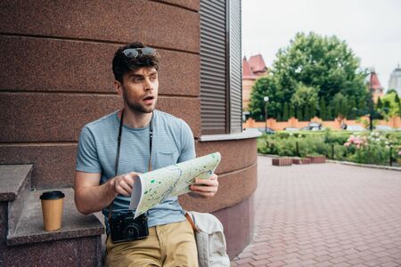 thoughtful and handsome man in glasses holding map and looking awayの写真素材