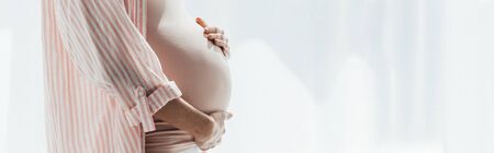 panoramic shot of pregnant woman in striped shirt touching bellyの写真素材