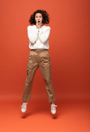shocked curly woman jumping on orange backgroundの写真素材