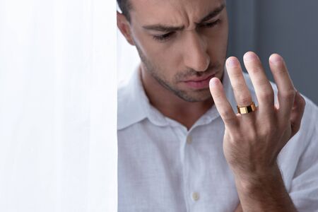 depressed man in white shirt looking on ring on finger