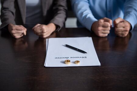 partial view of couple clenching fists at table with divorce documents