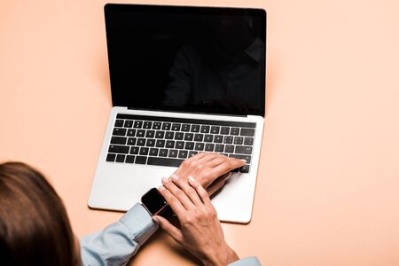 cropped view of woman touching smart watch near laptop with blank screen on pink