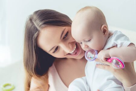 attractive and smiling mother holding her child in apartment