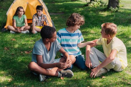 selective focus of multicultural boys sitting on grassの写真素材