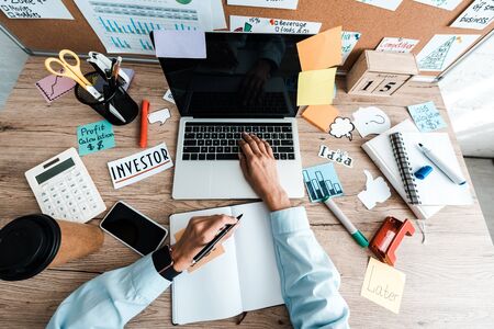top view of businesswoman holding pen near notebook and laptop with blank screen