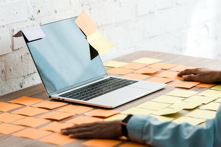 selective focus of woman sitting near laptop with blank screen and sticky notesの写真素材