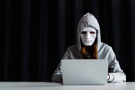 anonymous internet troll in mask typing on laptop keyboard on black