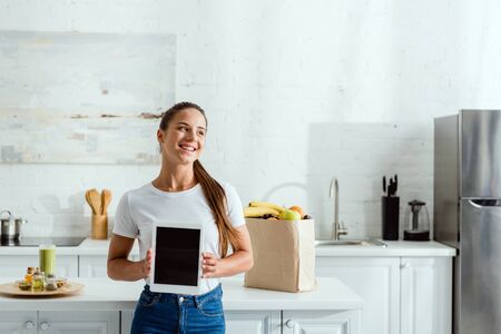 cheerful girl holding digital tablet with blank screen near groceriesの写真素材