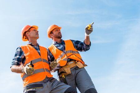 low angle view of handsome constructor pointing with finger while standing against blue skyの写真素材