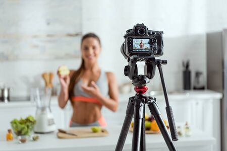 selective focus of digital camera with happy woman holding half of apple and gesturing on screenの写真素材