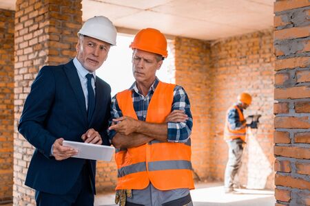 selective focus of businessman standing near builder pointing with finger at digital tablet