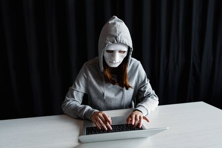 anonymous internet troll in mask typing on laptop keyboard on black