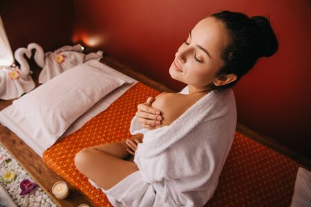 high angle view of attractive woman in bathrobe sitting on massage mat in spa salonの写真素材