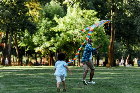 selective focus of happy african american father looking at son while running with kiteの写真素材