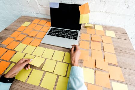 cropped view of woman near sticky notes and laptop with blank screen on desk