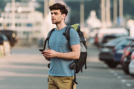 handsome man in t-shirt holding smartphone and looking awayの写真素材