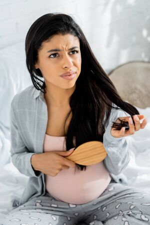 angry american pregnant woman in pajamas holding hairbrush in apartmentの写真素材